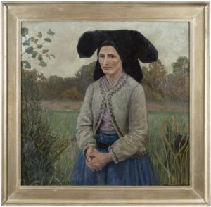 Frau in wendischer Alltagstracht mit schwarzer Haube, grauer Jacke und blauer Schürze steht vor einer Landschaft mit Bäumen und Feldern.